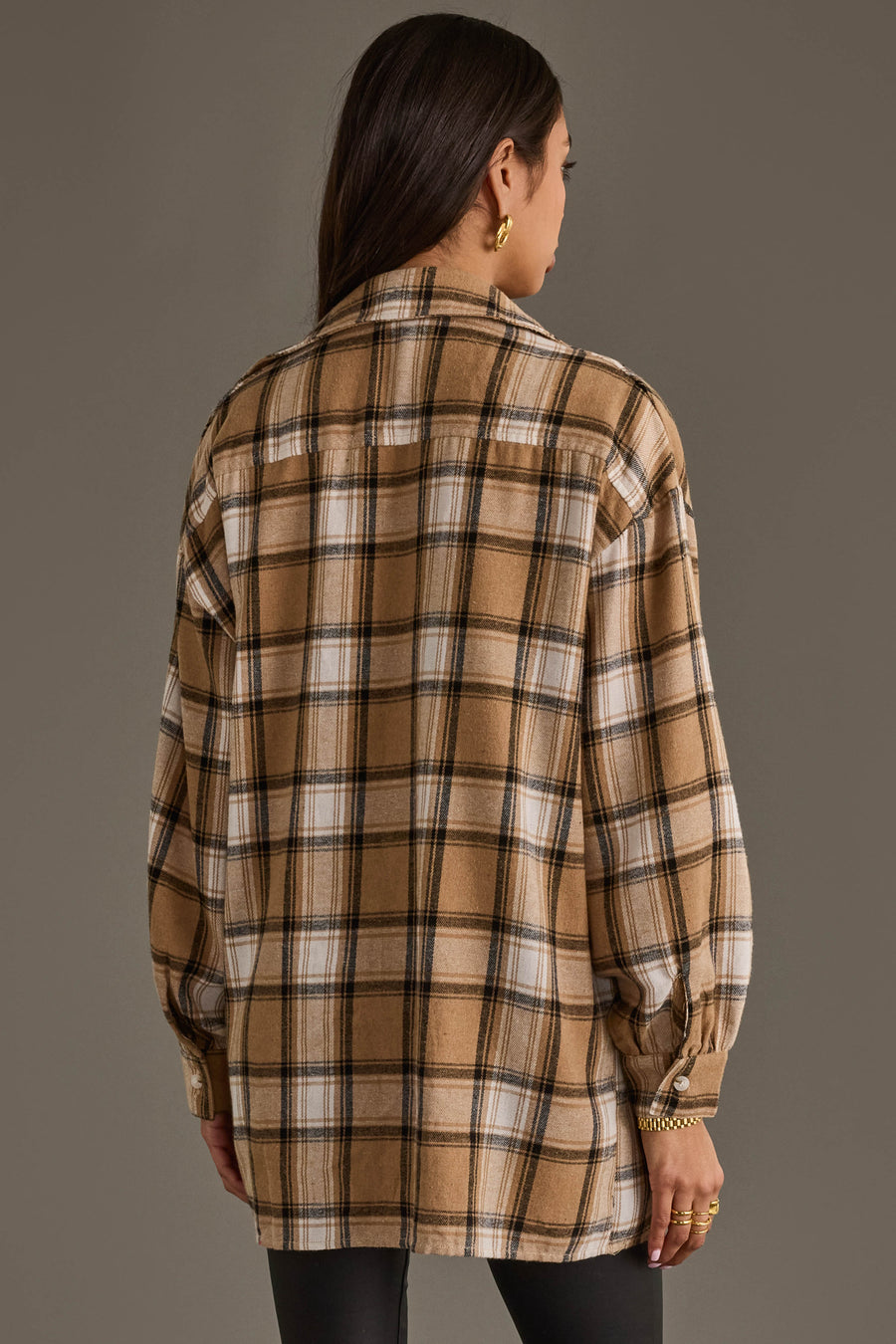 A person with long brown hair is seen from behind wearing the Panache Apparel Collection’s Tan, Black & White Boyfriend Fit Plaid Button Up with black pants, standing against a plain gray background.