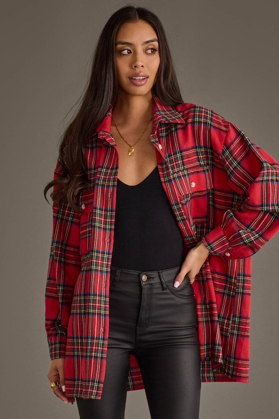 A woman stands against a plain background, wearing the Red Multicolored Boyfriend Flannel Button Up from Panache Apparel Collection over a black top and black pants. Her long hair is down, and she rests one hand on her hip.