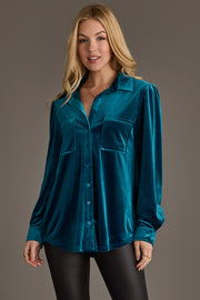 A woman wears the Dark Teal Velvet Button Up from Panache Apparel Collection with black pants, standing against a plain brown background and smiling softly at the camera.