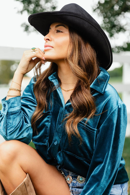 A woman wearing a relaxed fit, dark teal Dark Teal Velvet Button Up shirt and a black cowboy hat.