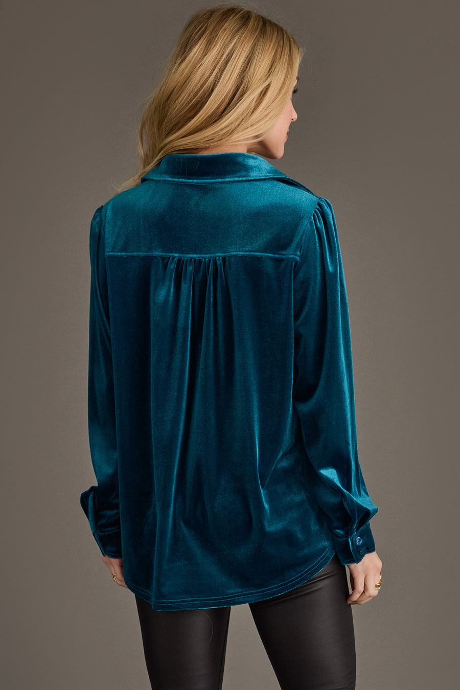 A woman with long blonde hair, seen from behind, wears the Panache Apparel Collection Dark Teal Velvet Button Up and black pants against a plain brown background.
