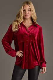 Model wears the Burgundy Velvet Button Up by Panache Apparel Collection with black pants, standing against a gray backdrop, smiling slightly with long loose blonde waves.