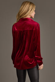A woman with long blonde hair models the Panache Apparel Collection Burgundy Velvet Button Up and black pants, standing with her back to the camera against a plain background.