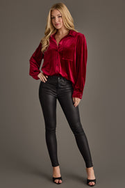A woman poses confidently in the Burgundy Velvet Button Up by Panache Apparel Collection, paired with black high-waisted skinny jeans and black open-toe heels.