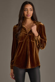 Woman with long dark hair wearing the Panache Apparel Collection Bronze Velvet Button Up, black pants, and gold jewelry, standing against a plain gray background and looking slightly to the side with a neutral expression.