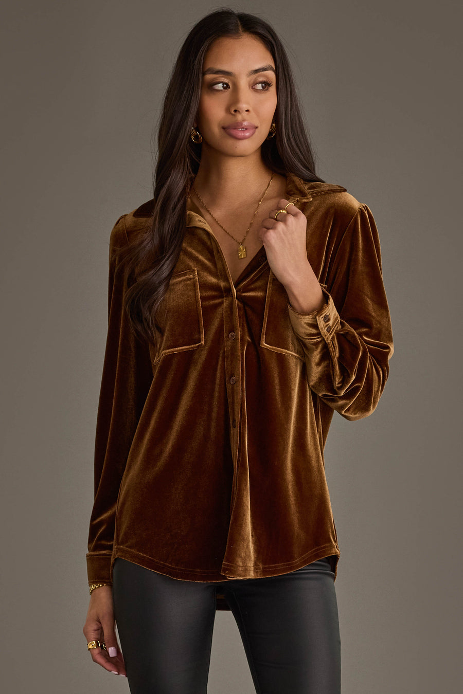 Woman with long dark hair wearing the Panache Apparel Collection Bronze Velvet Button Up, black pants, and gold jewelry, standing against a plain gray background and looking slightly to the side with a neutral expression.