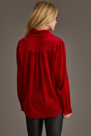 A woman with blonde hair is seen from behind wearing the Red Velvet Button Up by Panache Apparel Collection and black pants, standing against a plain gray background.