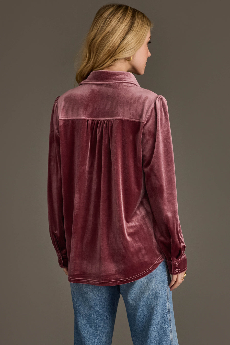 A woman with blonde hair models the Mauve Velvet Button Up by Panache Apparel Collection, paired with blue jeans, facing away from the camera against a plain background.