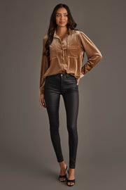 A woman with long dark hair smiles slightly, wearing the Tan Velvet Button Up from Panache Apparel Collection, black skinny pants, and black open-toe heels against a plain gray background.