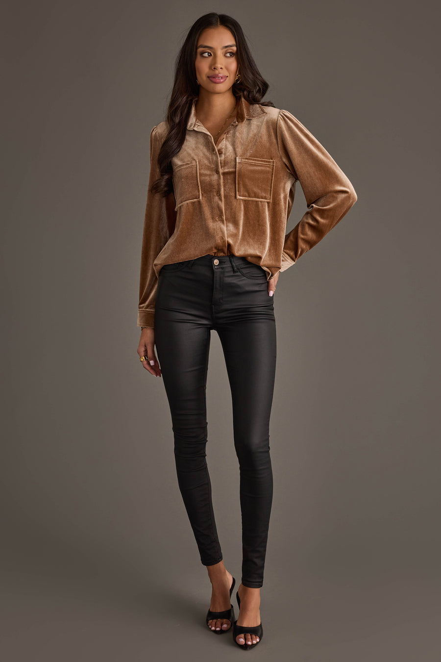 A woman with long dark hair smiles slightly, wearing the Tan Velvet Button Up from Panache Apparel Collection, black skinny pants, and black open-toe heels against a plain gray background.