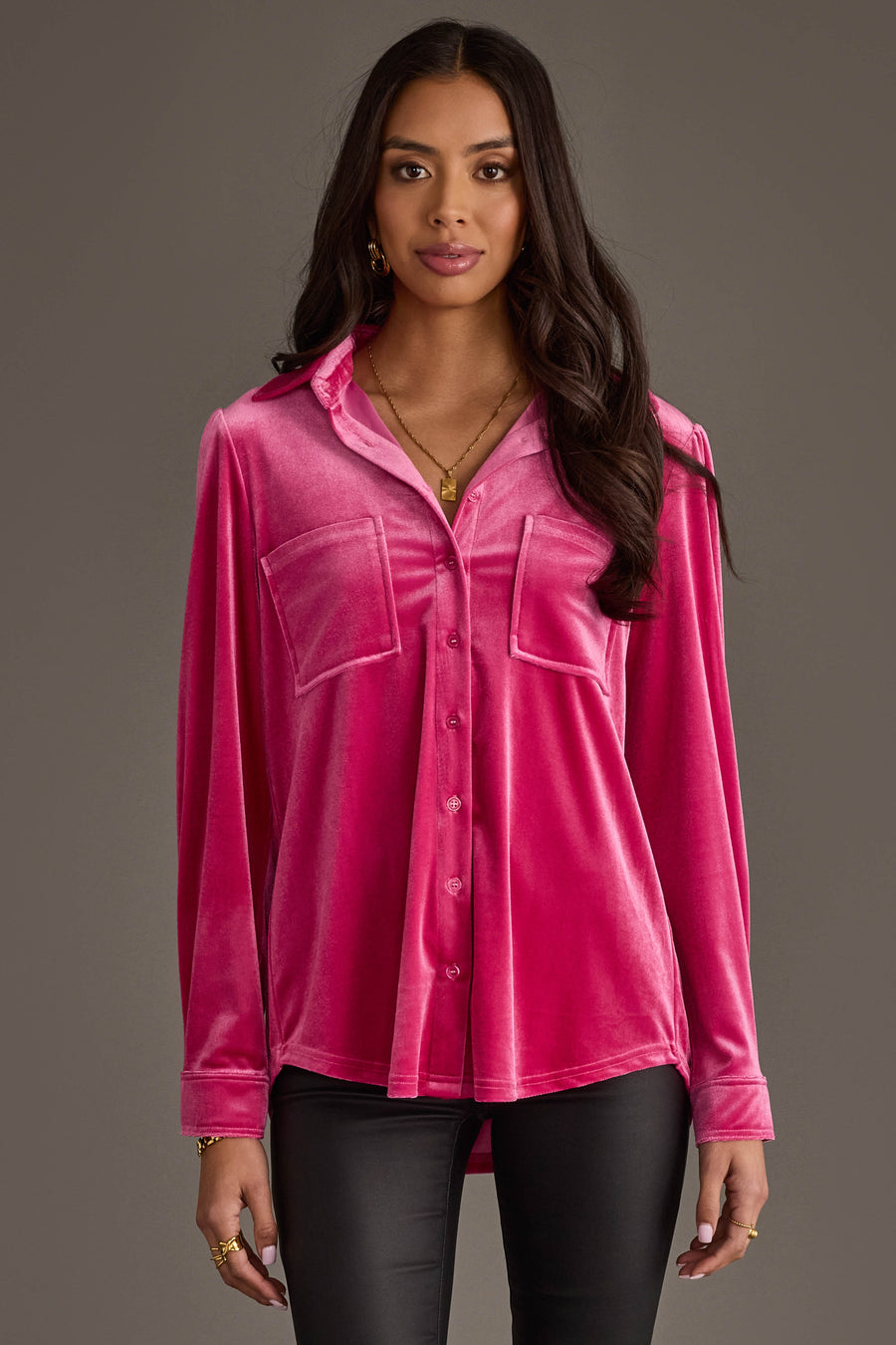 A woman in the Panache Apparel Collection Bright Pink Velvet Button Up with two front pockets and black pants stands against a gray background, looking forward with a neutral expression.