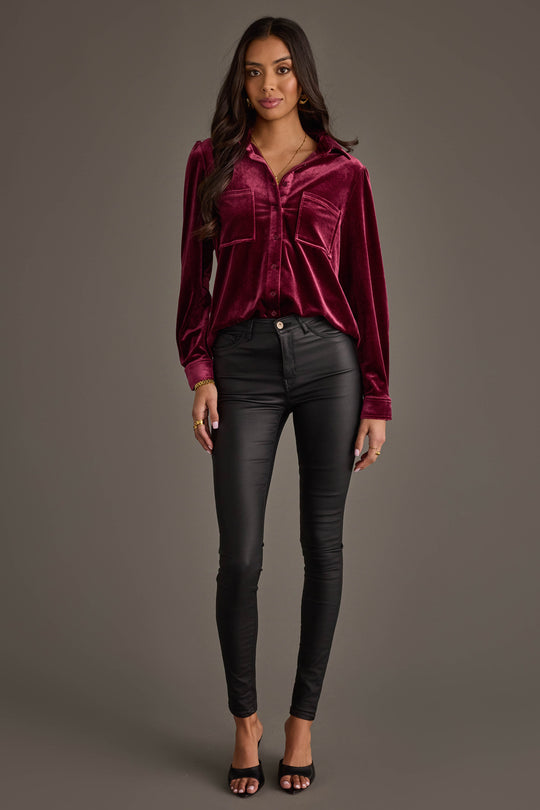 Woman with long wavy hair stands against a plain background, wearing the Panache Apparel Collection Maroon Velvet Button Up, black skinny pants, and black open-toe heels. She looks forward with a neutral expression.