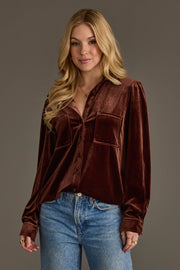 A woman with long blonde hair smiles softly at the camera, wearing the Panache Apparel Collection Brown Velvet Button Up and blue jeans against a plain gray background.