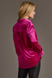 A woman in the Panache Apparel Collection Fuchsia Velvet Button Up and black pants faces away, highlighting the blouse’s back against a plain gray background.