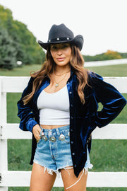 A woman wears a relaxed fit Navy Velvet Button Up from Panache Apparel Collection over a white ribbed tank top and denim shorts, accessorized with a black cowboy hat.