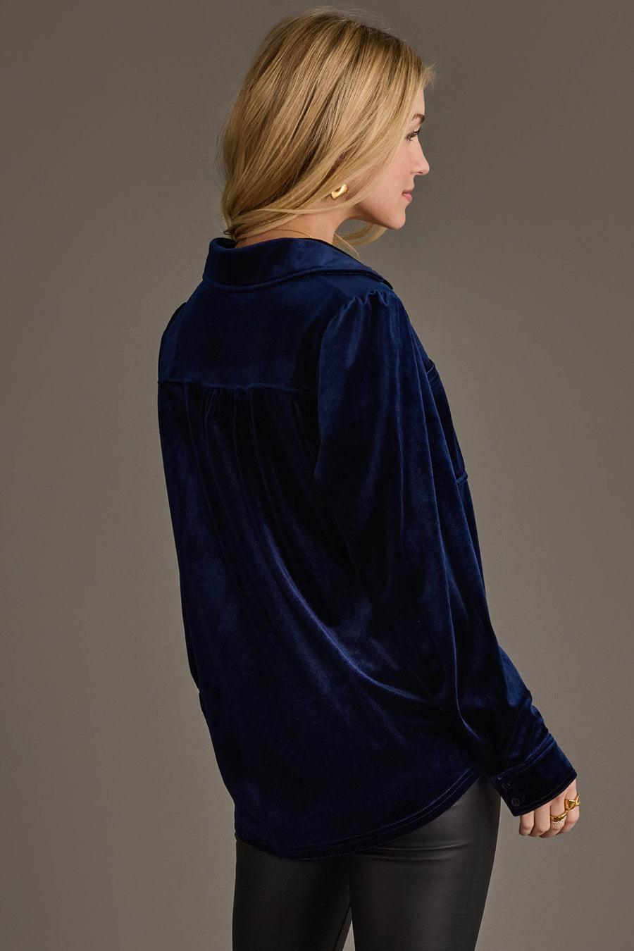 A woman with long blonde hair models the Panache Apparel Collection Navy Velvet Button Up with black pants, standing sideways and looking left against a plain brown background.