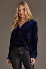 A woman with long blonde hair wears the Navy Velvet Button Up from Panache Apparel Collection and black leather pants, standing against a gray background and smiling slightly at the camera.