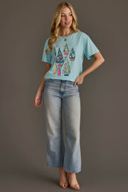 A woman wearing a Light Blue Christmas Trees Tee paired with wide-leg light-wash jeans.
