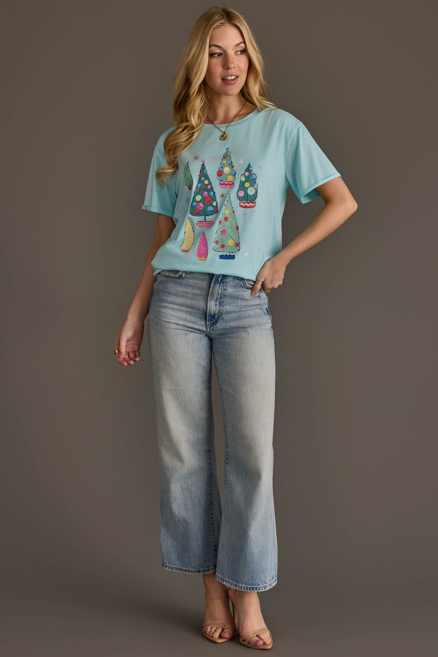 A woman wearing a Light Blue Christmas Trees Tee paired with wide-leg light-wash jeans.