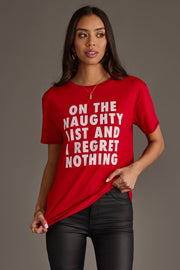 A person wearing a relaxed fit, red On The Naughty List Tee from the Panache Apparel Collection that reads On the naughty list and I regret nothing in white block letters.