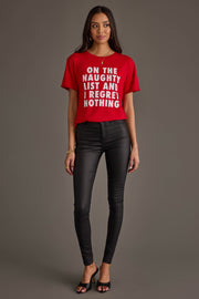 A woman wearing the On The Naughty List Tee in a relaxed fit red with white text paired with black skinny pants.