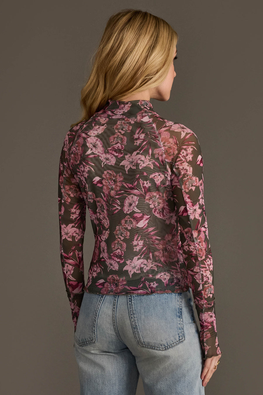 A person with long blonde hair, facing away from the camera, wears the Panache Apparel Collection Olive & Pink Floral Mesh Top paired with light blue jeans.