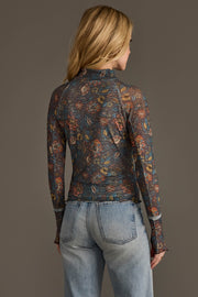 A woman with long blonde hair, seen from the back, wears the Panache Apparel Collection Gray, Orange & Blue Floral Mesh Top and light blue jeans against a plain, neutral background.