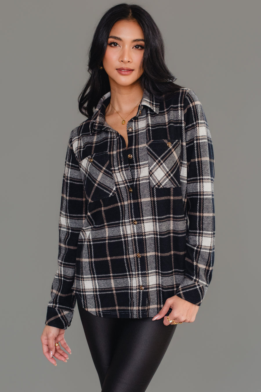 A woman wearing the Panache Apparel Collection Black, White & Tan Plaid Button Up and black pants stands against a plain gray background, looking at the camera with a slight smile and relaxed pose.