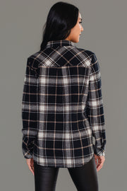 A woman with long dark hair faces away, wearing the Panache Apparel Collection Black, White & Tan Plaid Button Up paired with black pants against a plain grey background.