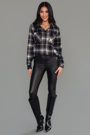 A woman stands smiling, wearing the Panache Apparel Collection Black, White & Tan Plaid Button Up, paired with black leather pants and tall black boots against a plain gray background.