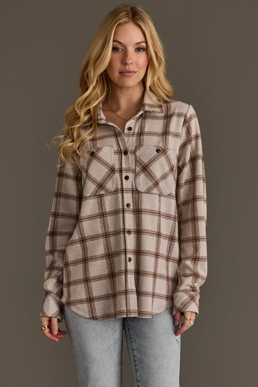 A woman with long blonde hair models the Panache Apparel Collection Light Taupe & Brown Plaid Button Up, paired with light blue jeans, standing against a plain gray background.