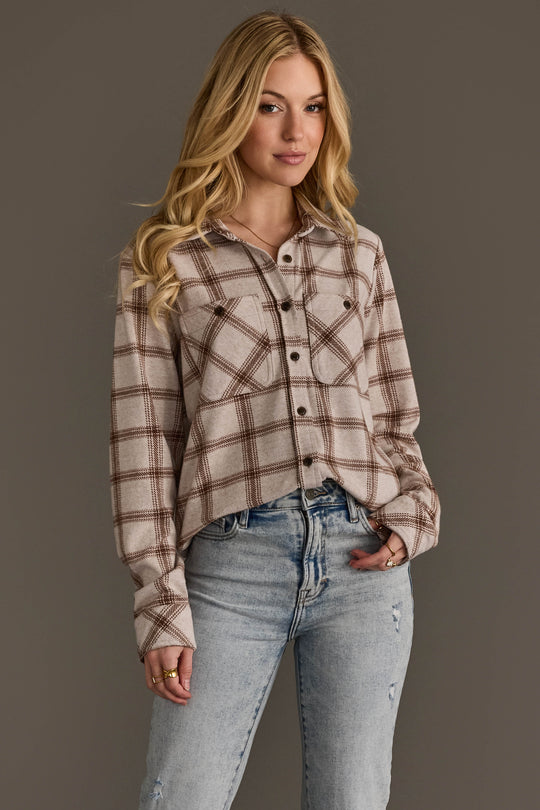 A woman with long blonde hair is wearing the Panache Apparel Collection Light Taupe & Brown Plaid Button Up and light blue ripped jeans, standing against a plain gray background.