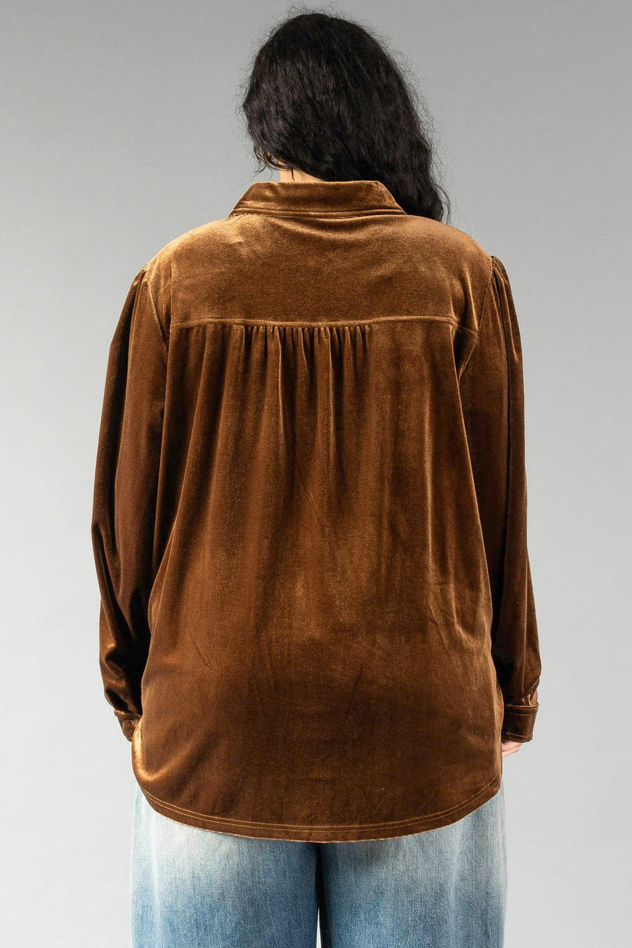 Back view of the Bronze Velvet Button Up in bronze velvet, featuring a pleated back yoke and worn with light wash jeans.