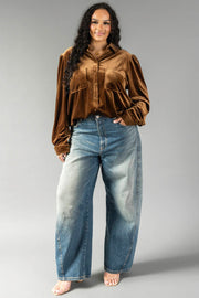A person wearing a long-sleeved Bronze Velvet Button Up tucked into wide-leg blue jeans.