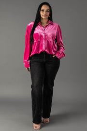 A person wearing a bright pink velvet Bright Pink Velvet Button Up blouse with two chest pockets and black denim jeans.