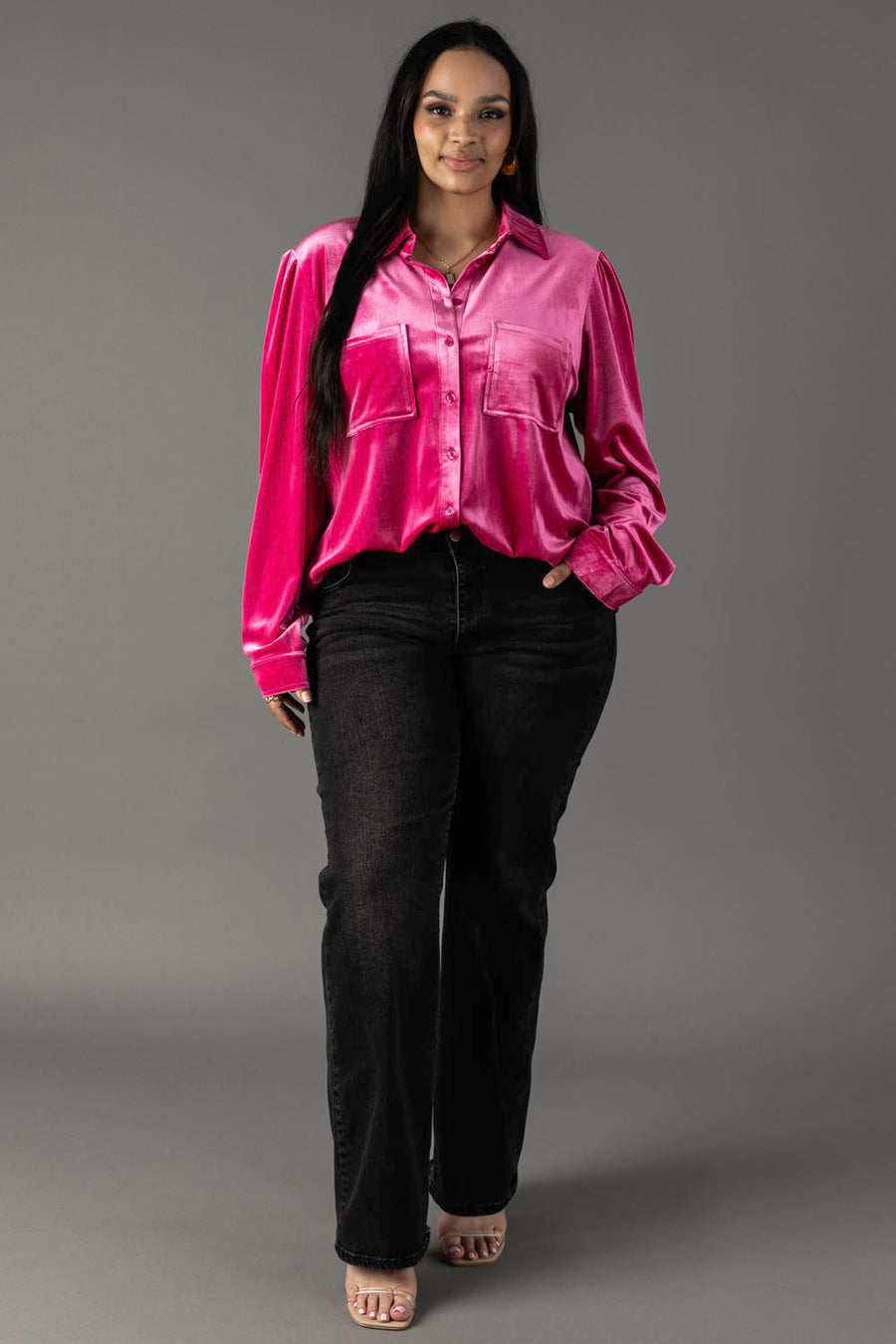 A person wearing a bright pink velvet Bright Pink Velvet Button Up blouse with two chest pockets and black denim jeans.