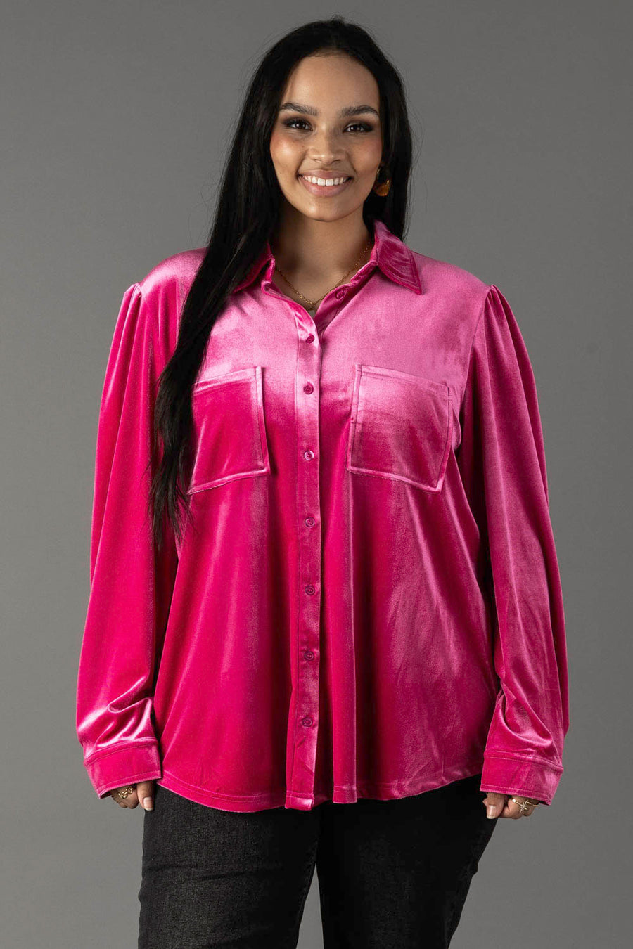 A smiling woman wearing a bright pink Bright Pink Velvet Button Up blouse with two front pockets.