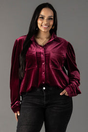 A smiling woman wears a long-sleeved maroon velvet button-up shirt from the Panache Apparel Collection featuring two chest pockets, paired with black jeans.