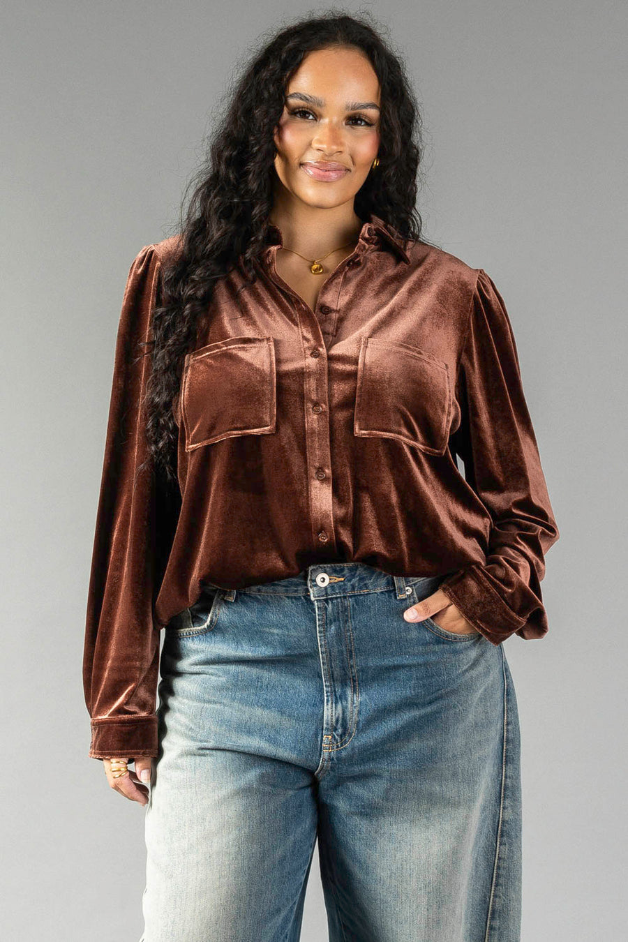 A person wears a brown velvet Brown Velvet Button Up with two front chest pockets and blue jeans.
