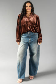A person wearing a long-sleeved brown velvet Brown Velvet Button Up with chest pockets and loose-fitting blue jeans.