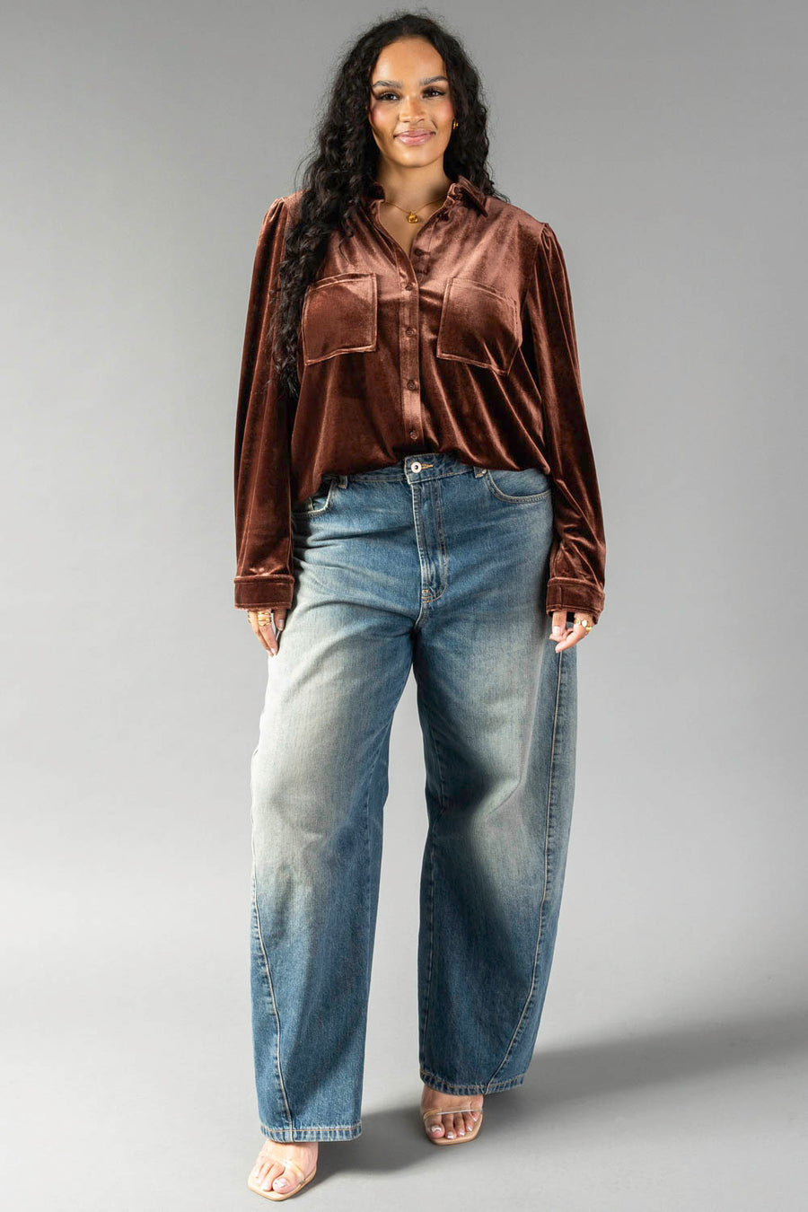 A person wearing a long-sleeved brown velvet Brown Velvet Button Up with chest pockets and loose-fitting blue jeans.