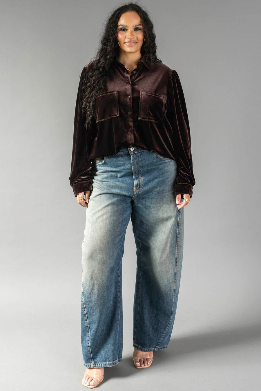 A woman wearing a long-sleeved, espresso brown velvet Espresso Brown Velvet Button Up shirt with two front pockets and wide-leg blue jeans.