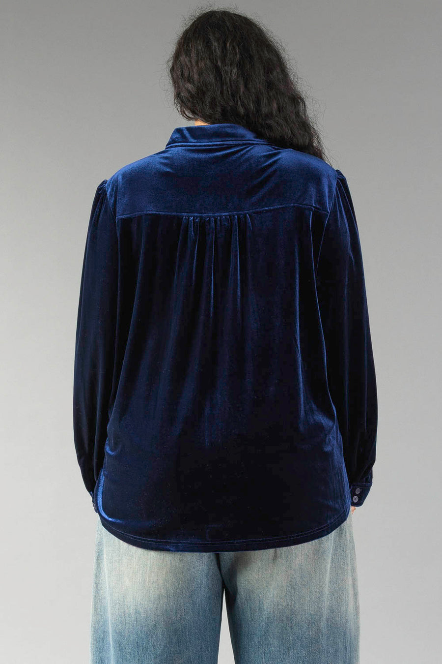 Back view of a Navy Velvet Button Up in a relaxed fit navy blue velvet with a gathered yoke, worn with light wash jeans.