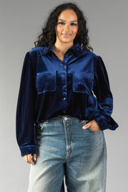 A woman wearing a Navy Velvet Button Up in navy velvet with long sleeves, two front chest pockets, and blue jeans.