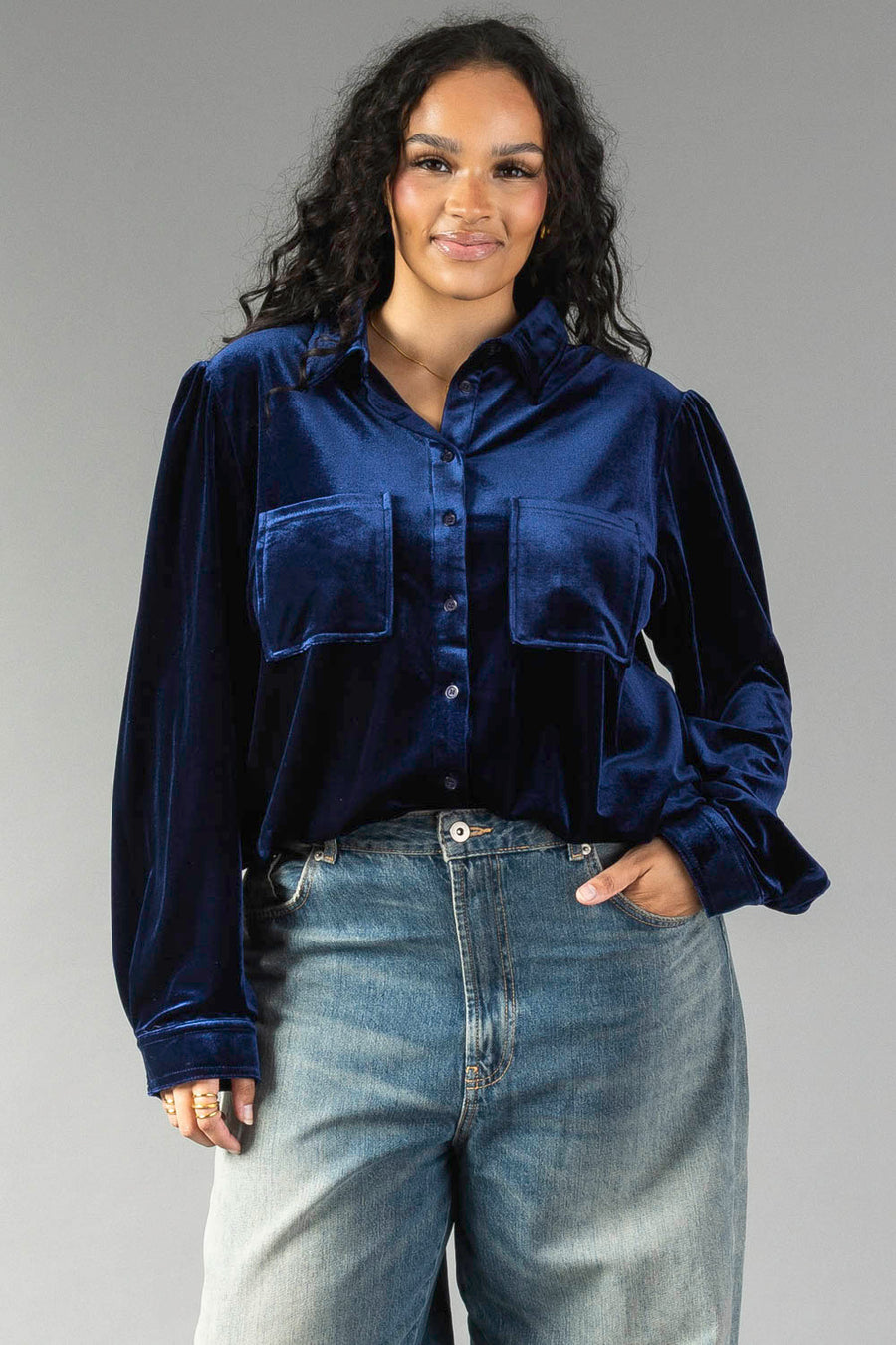 A woman wearing a Navy Velvet Button Up in navy velvet with long sleeves, two front chest pockets, and blue jeans.