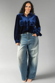 A person wearing a Navy Velvet Button Up in navy long-sleeved velvet paired with loose-fitting blue jeans.