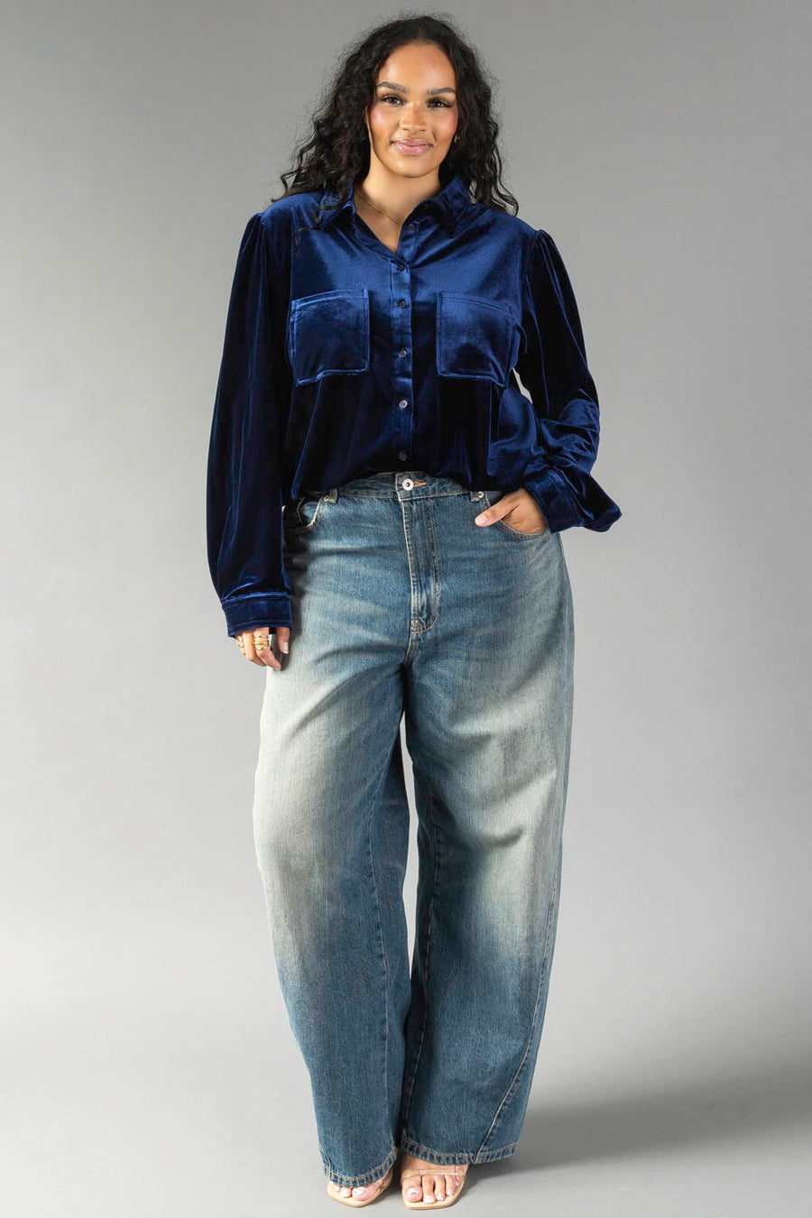 A person wearing a Navy Velvet Button Up in navy long-sleeved velvet paired with loose-fitting blue jeans.