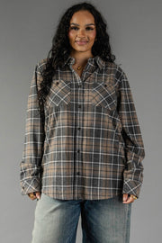 A woman with long curly hair wears the Panache Apparel Collection Gray, Tan & White Plaid Button Up and light blue jeans, standing against a plain gray background and smiling slightly.