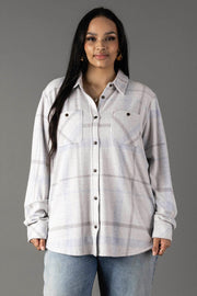 A woman with long dark hair wears the Panache Apparel Collection White, Gray & Light Blue Plaid Button Up, featuring two chest pockets, paired with light blue jeans as she stands against a plain gray background.