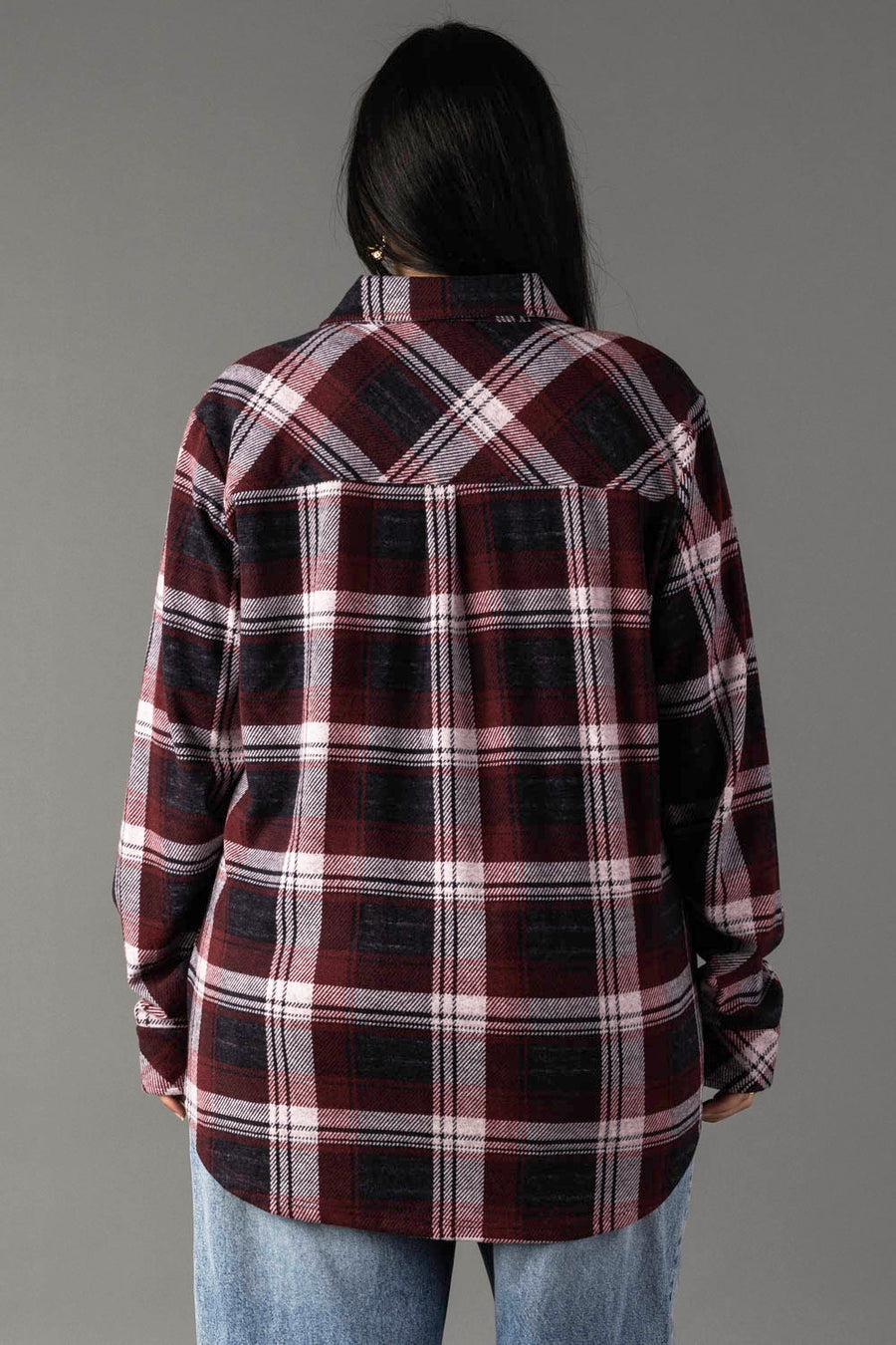 A person with long dark hair, seen from behind against a plain gray background, is wearing the Panache Apparel Collection’s Maroon, Charcoal & White Plaid Button Up and light blue jeans.